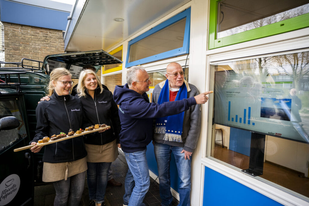 Wethouder Duurzaamheid Nico van Veen kijkt samen met een vrijwilliger van Zonkracht Capelle naar het dashboard met de opgewekte enerige