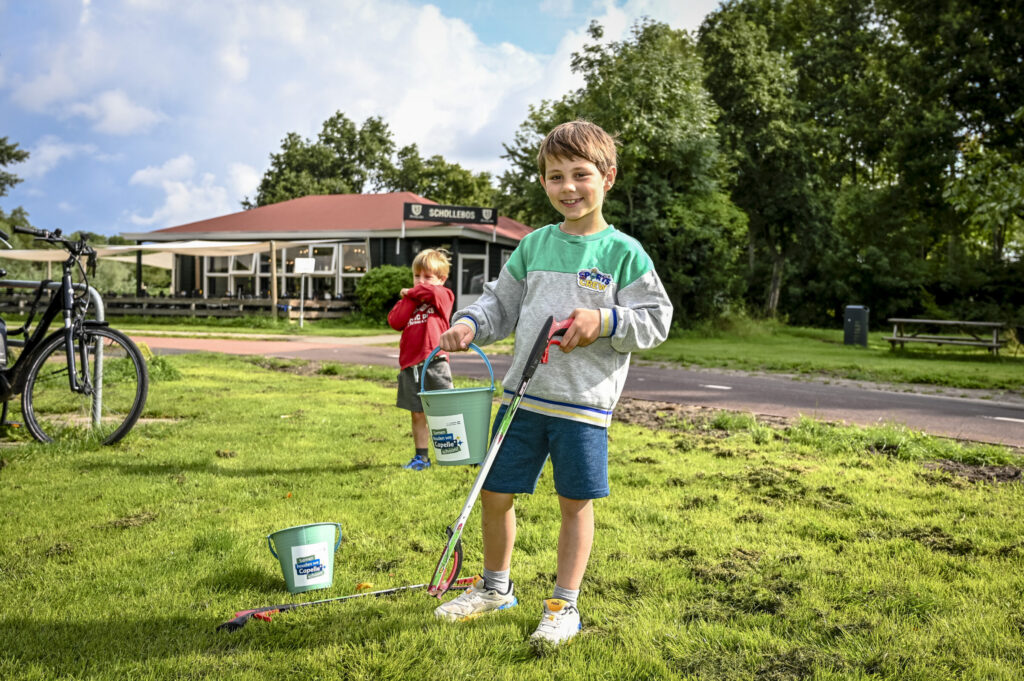 Kindje raapt afval met afvalprikker en doet het in zijn emmer