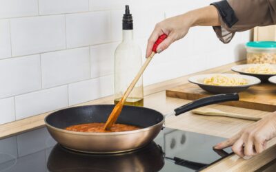 Iemand roert in een koekenpan die op een inductiekookplaat staat.