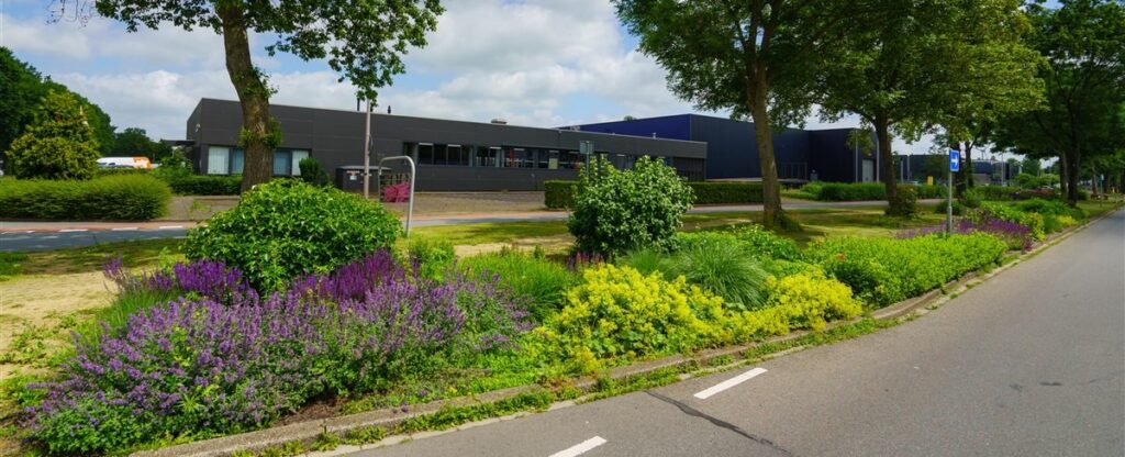 Bedrijfspand met veel groene beplanting ervoor.