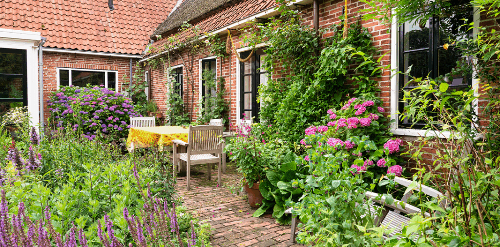 Tuin met een houten tafel en stoelen en veel planten.