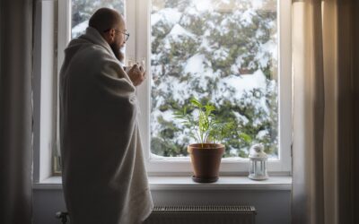 Man staat met deken om voor het raam. Buiten ligt sneeuw.