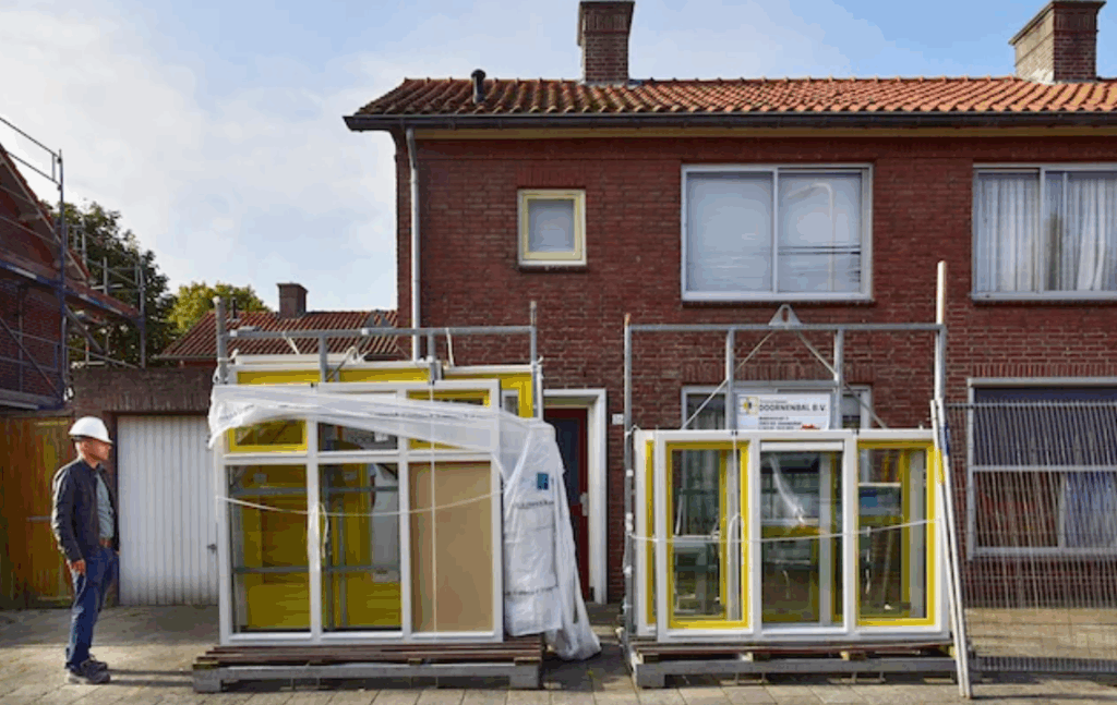 Een wat ouder rijtjeshuis wordt gerenoveerd. Voor het huis staan nieuwe ramen klaar.