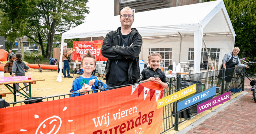 Organisator van de burendag met twee kinderen die aanwezig waren. Ze poseren bij de vlag van Burendag