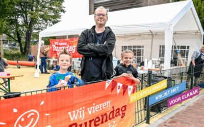 Organisator van de burendag met twee kinderen die aanwezig waren. Ze poseren bij de vlag van Burendag