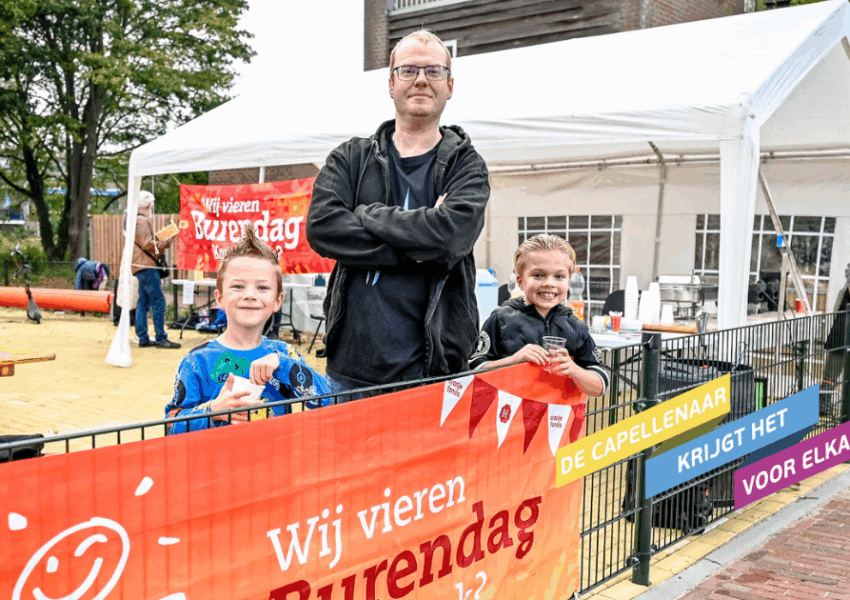Organisator van de burendag met twee kinderen die aanwezig waren. Ze poseren bij de vlag van Burendag