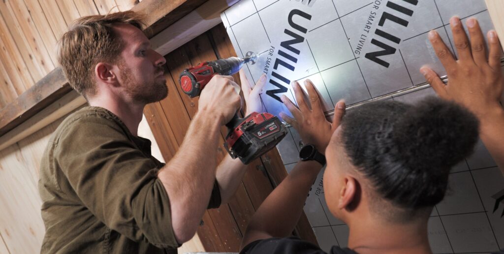 Twee jonge mannen monteren een plaat isolatiemateriaal aan het zolderdak.