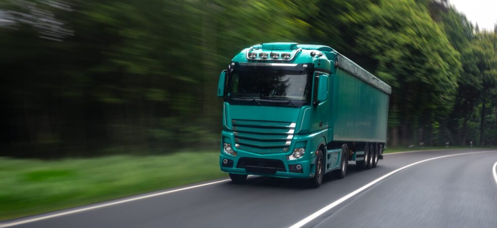 Groene vrachtwagen rijdt op de snelweg door een bosachtige omgeving.