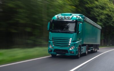 Groene vrachtwagen rijdt op de snelweg door een bosachtige omgeving.