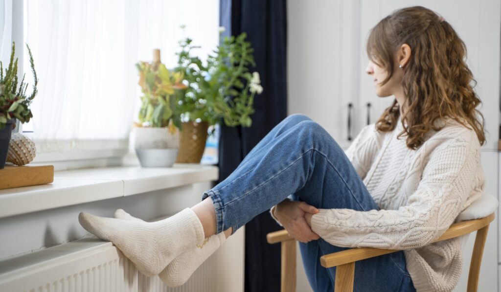 Vrouw zit met haar voeten op de verwarming.
