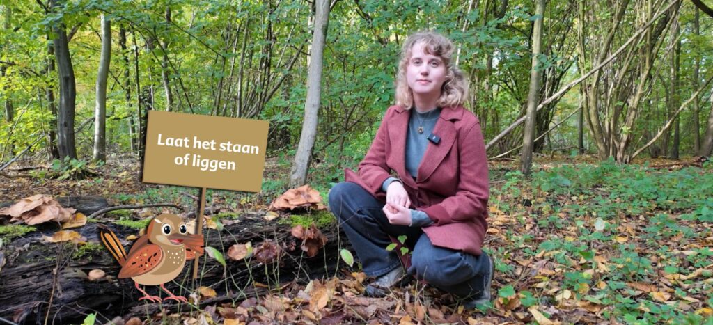 Tessa bij een dode boom. Met het winterkoninkje erbij die een bord vast heeft met de tekst 'laat het staan of liggen'