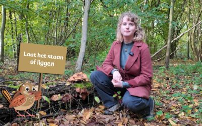 Tessa bij een dode boom. Met het winterkoninkje erbij die een bord vast heeft met de tekst 'laat het staan of liggen'