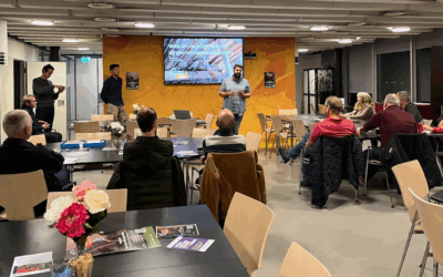Zaal vol mensen en iemand die een presentatie geeft.