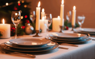 Gedekte tafel met borden, bestek en kaarsen. op de achtergrond zie je een stukje kerstboom