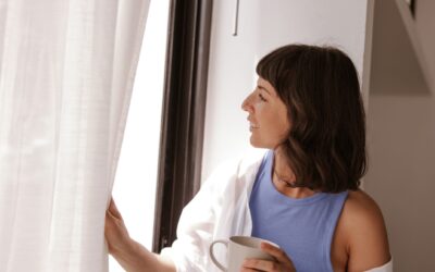 Vrouw staat voor het raam met kop koffie in haar hand.