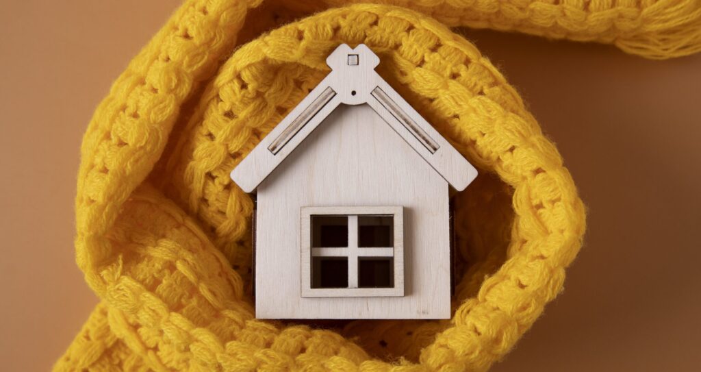 Houten speelgoedhuisje met een sjaal eromheen, om aan te tonen wat isolatie doet voor uw huis.
