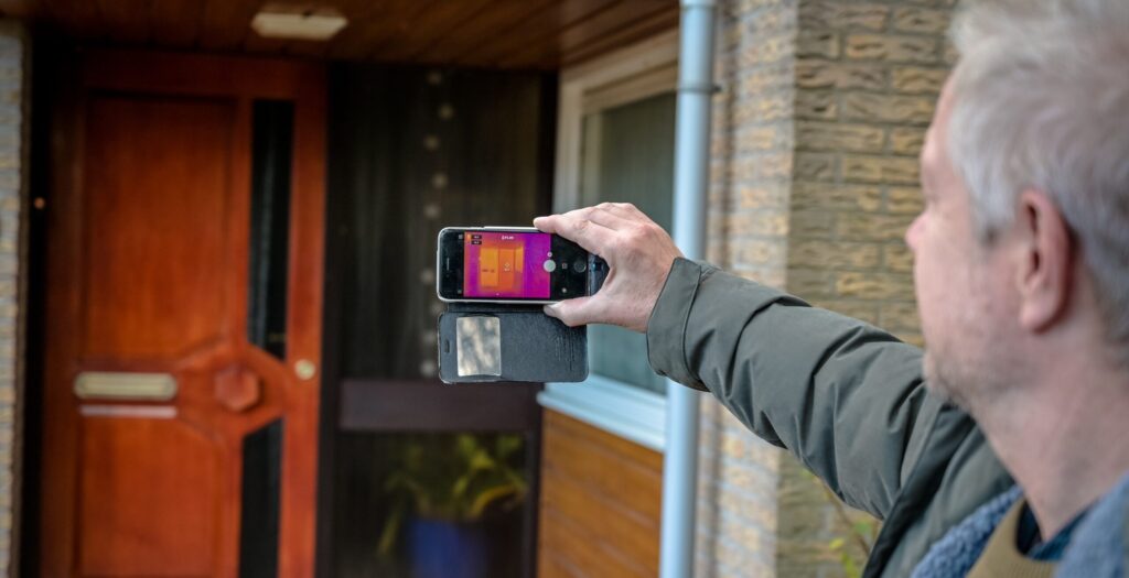 Man houdt een warmtecamera vast voor de voordeur van een huis.