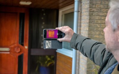 Man houdt een warmtecamera vast voor de voordeur van een huis.