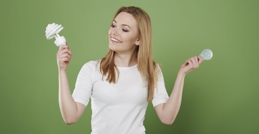 Een vrouwelijke energiecoach houdt 2 lampen omhoog: 1 led en 1 ouderwetse gloeilamp.