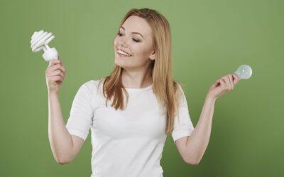 Een vrouwelijke energiecoach houdt 2 lampen omhoog: 1 led en 1 ouderwetse gloeilamp.
