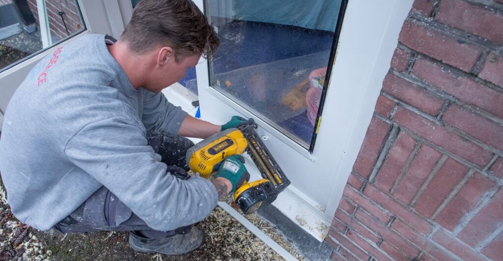 Man is op z'n hurken bezig isolatieglas in een tuindeur te plaatsen.