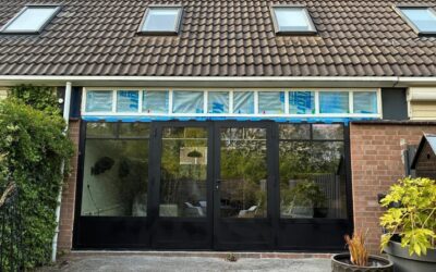 Gezien vanuit de tuin: net geplaatste zwarte kozijnen van openslaande deuren. Daarboven is nog isolatiemateriaal zichtbaar.