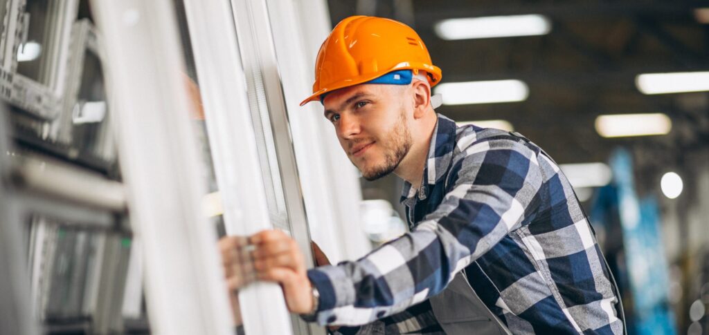 Jonge man met oranje veiligheidshelm staat bij ramen en kozijnen.