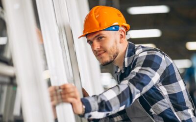 Jonge man met oranje veiligheidshelm staat bij ramen en kozijnen.