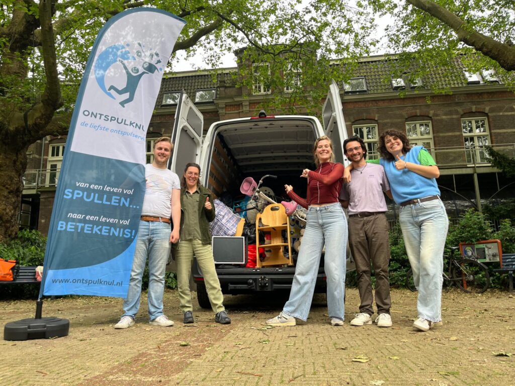 Medewerkers van Ontspulknul staan bij hun bus met een beachvlag erbij