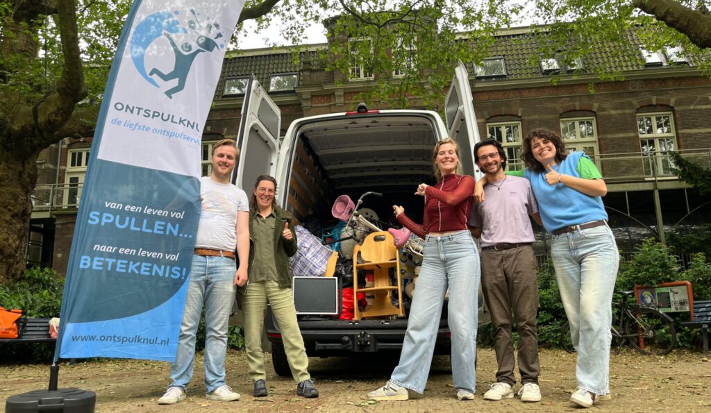 Medewerkers van Ontspulknul staan bij hun bus met een beachvlag erbij