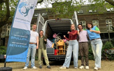 Medewerkers van Ontspulknul staan bij hun bus met een beachvlag erbij