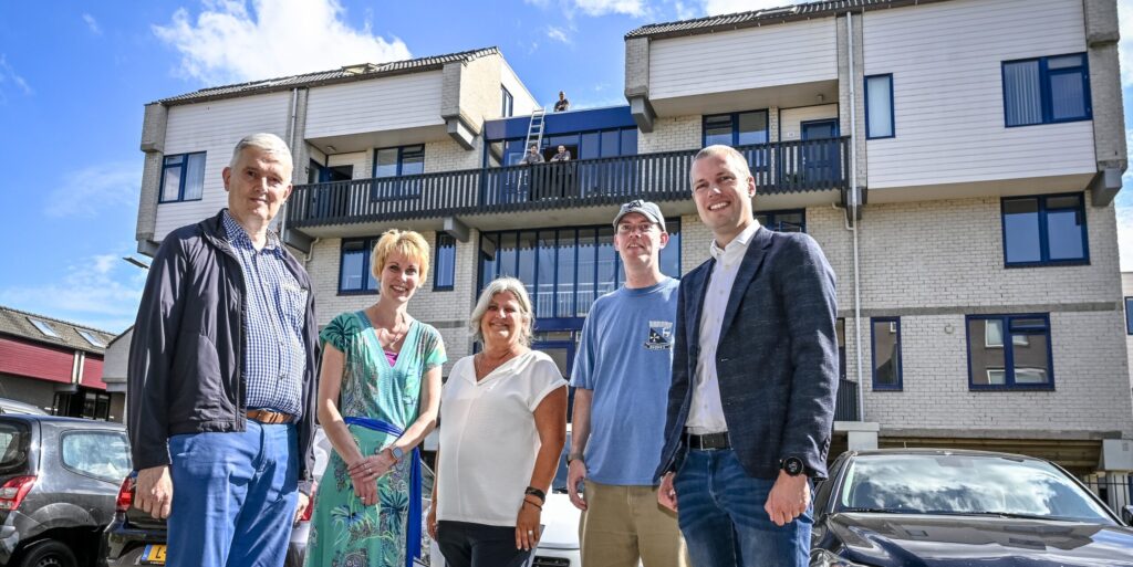 VvE-leden staan voor hun flatgebouw waar zonnepanelen zijn geplaatst. Wethouder Sjoerd Geissler staat er ook bij.