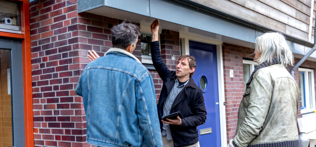 Buren kijken naar de buitenkant van hun pand. Een man voelt aan een muur.