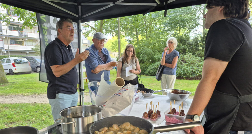 Kookeiland op een grasveld waar 5 mensen omheen staan die kijken, koken en vragen stellen.