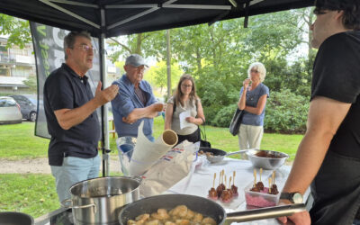 Kookeiland op een grasveld waar 5 mensen omheen staan die kijken, koken en vragen stellen.