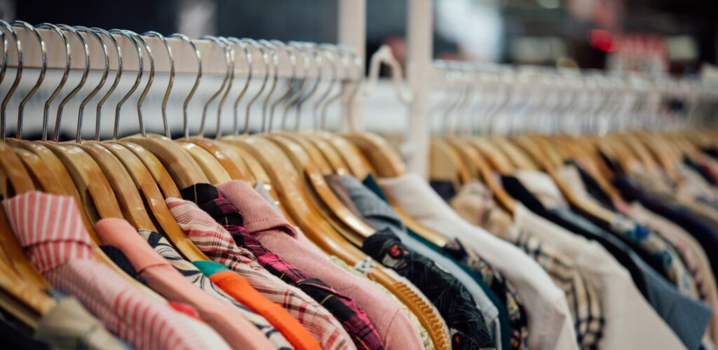 Kledingrek van dichtbij met veel hangertjes en overhemden daaraan.