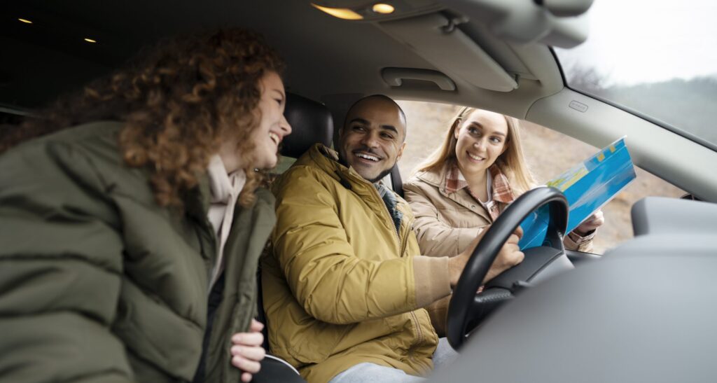 Twee jonge mensen in een auto. En iemand staat ernaast met een routekaart.